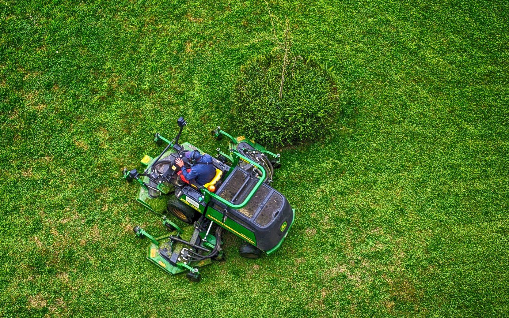 Rozbudowana kosiarka do koszenia trawy, na tle zielonego przystrzyżonego trawnika 